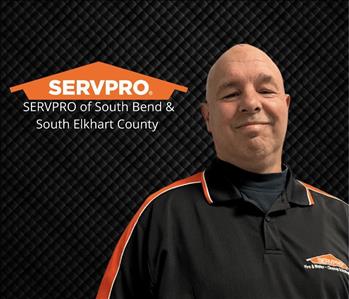bald man smiling at the camera with a black background and a SERVPRO logo