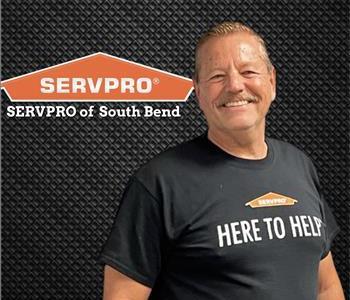 man smiling in a SERVPRO tee under a SERVPRO logo in front of a gray wall