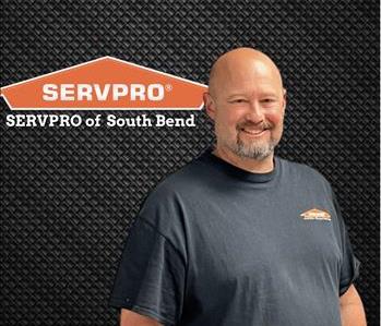 Man in black SERVPRO shirt smiling while under a SERVPRO logo